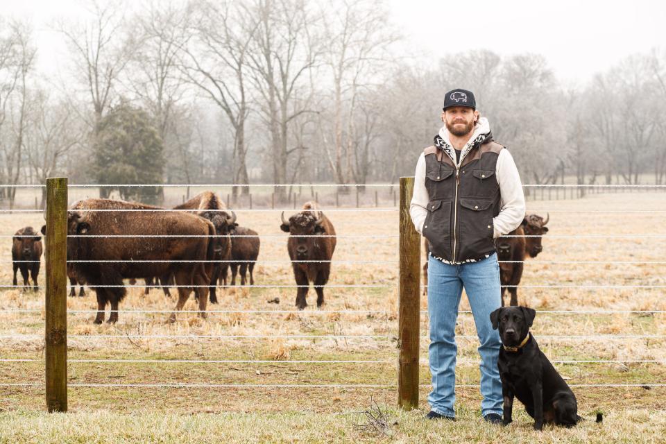 Chase Rice and his dog Jack, stand in front a heard of bison that are kept on his property in Franklin, Tenn. on Feb. 1, 2023.