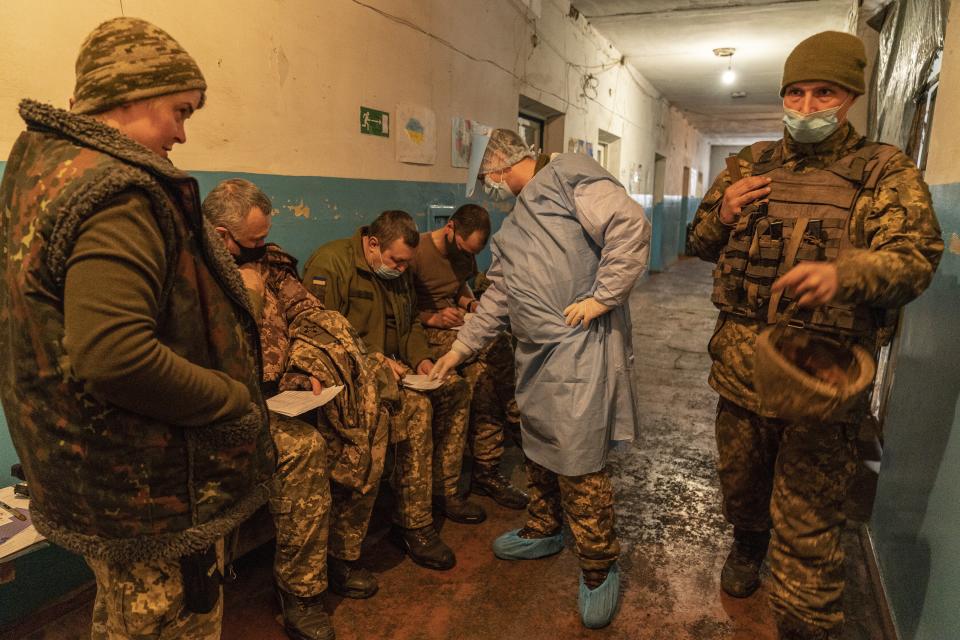 A Ukrainian military medic helps Ukrainian servicemen to fill in a medical form before receiving a dose of the AstraZeneca COVID-19 vaccine marketed under the name CoviShield at a military base near the front-line town of Krasnohorivka, eastern Ukraine, Friday, March 5, 2021. The country designated 14,000 doses of its first vaccine shipment for the military, especially those fighting Russia-backed separatists in the east. But only 1,030 troops have been vaccinated thus far. In the front-line town of Krasnohorivka, soldiers widely refuse to vaccinate. (AP Photo/Evgeniy Maloletka)