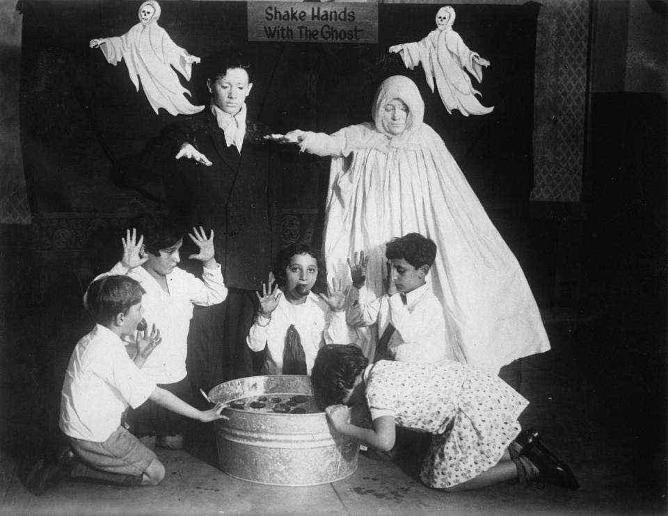 <p>Children surrounded by "ghosts" go bobbing for apples at a Halloween party around 1935.</p>