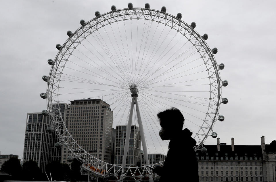 A man wears a face mask as he passes the London Eye in London, Thursday, Oct. 29, 2020. The International Monetary Fund has downgraded its growth forecasts for the British economy for this year and next, in its annual assessment published Thursday, following an acceleration in the number of coronavirus infections over the past couple of weeks.(AP Photo/Frank Augstein)