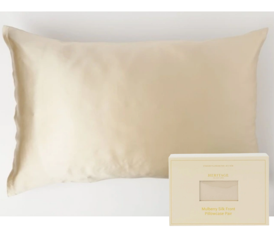 A champagne silk pillow sits flat lay on a pale grey background with the matching champage coloured box sits on the bottom right.