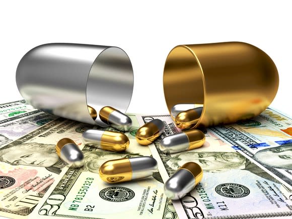 Gold and silver pills spill out of a bigger gold and silver pill onto $10, $20, and $50 bills.