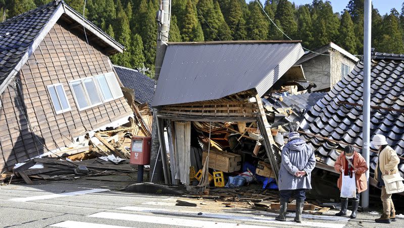 People look at collapsed buildings following an earthquake in Wajima, Ishikawa prefecture, Japan, Tuesday, Jan. 2, 2024. A series of powerful earthquakes in western Japan damaged homes, cars and boats, with officials warning people on Tuesday to stay away from their homes in some areas because of a continuing risk of major quakes and tsunamis.