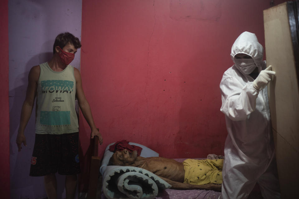 A worker from the SOS Funeral service, wearing protective gear amid the new coronavirus pandemic, is helped by caregiver Leandro Beiton as he prepares to remove the body of Edgar Silva in Manaus, Brazil, Tuesday, May 12, 2020. According to Silva's relatives, the elderly man had Alzheimer's and died at home after two days of fever and difficulty breathing. (AP Photo/Felipe Dana)