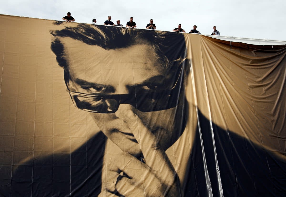 Workers set up a giant canvas of the official poster of the 67th Cannes, featuring late actor Marcello Mastroianni on the Festival Palace on 12 May 2014 (Reuters)