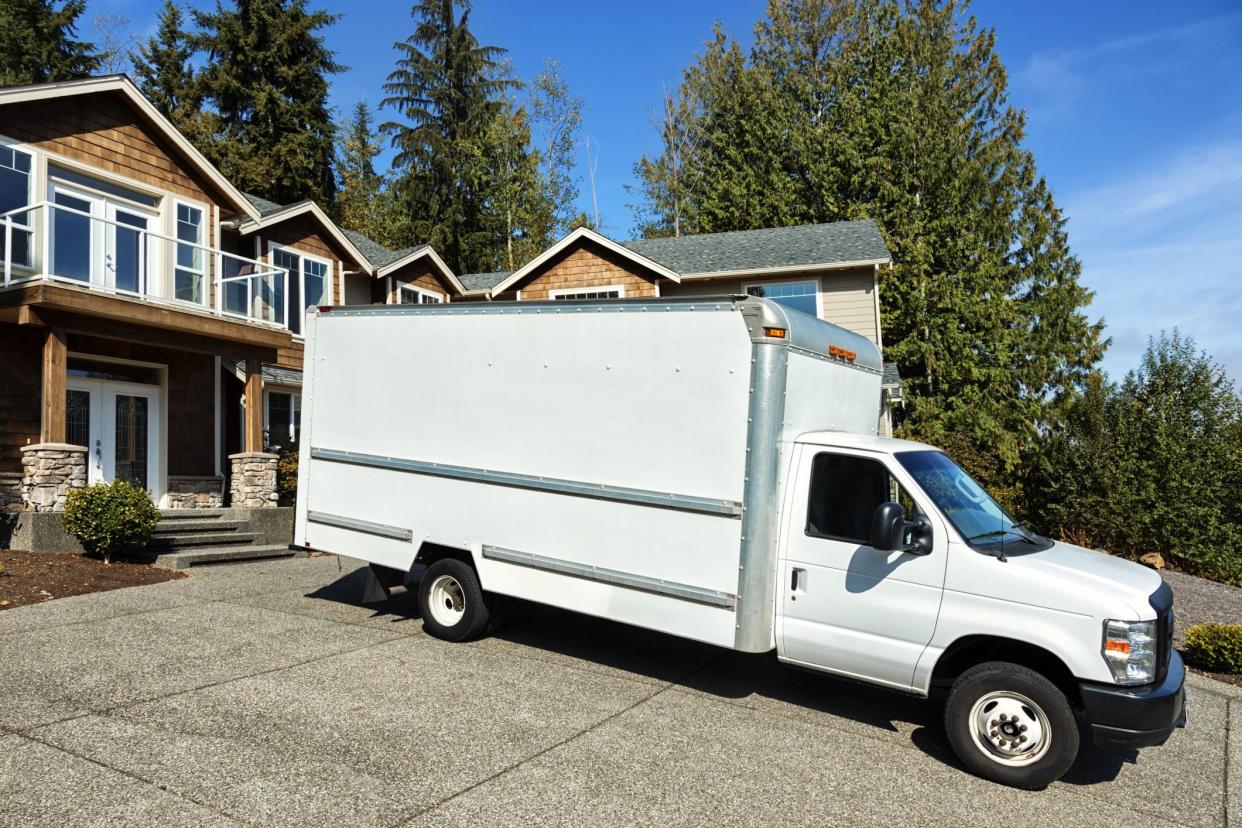 Photo of a plain white moving truck parked in the driveway of a modern home.