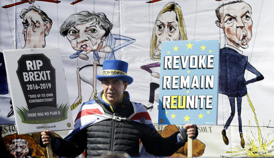 Anti-Brexit demonstrator Steve Bray stands in front of a banner held by pro-Brexit demonstrators near Parliament in London, Wednesday, April 10, 2019.  Just days away from a no-deal Brexit, European Union leaders meet Wednesday to discuss granting the United Kingdom a new delay to its departure from the bloc. (AP Photo/Kirsty Wigglesworth)