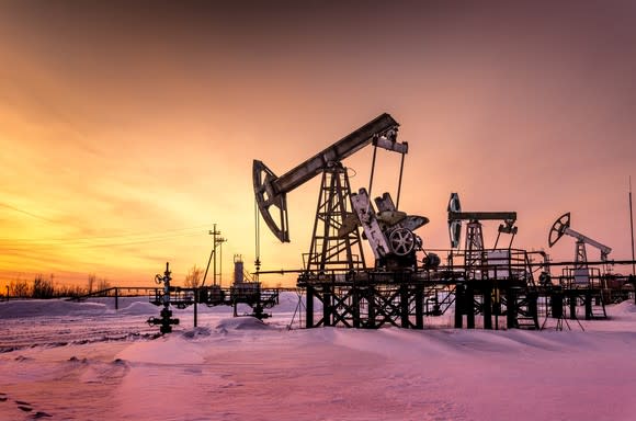 A oil pump at sunset with snow on the ground.