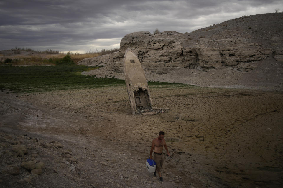 Un hombre pasa cerca de una embarcación hundida en el barro en la orilla del Lago Mead, cerca de Boulder City, en Nevada, el 22 de junio de 2022. (AP Foto/John Locher)