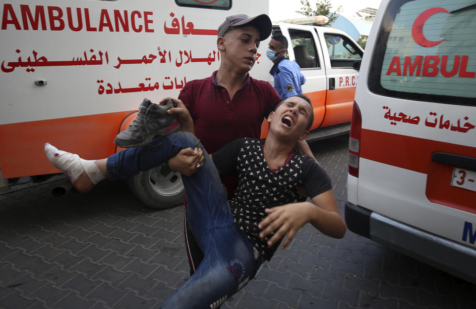 A protestor helps a wounded youth, who was shot by Israeli troops in his foot during a protest at the Gaza Strip's border with Israel, into the treatment room of Shifa hospital in Gaza City, Saturday, Aug. 21, 2021. (AP Photo/Abdel Kareem Hana)