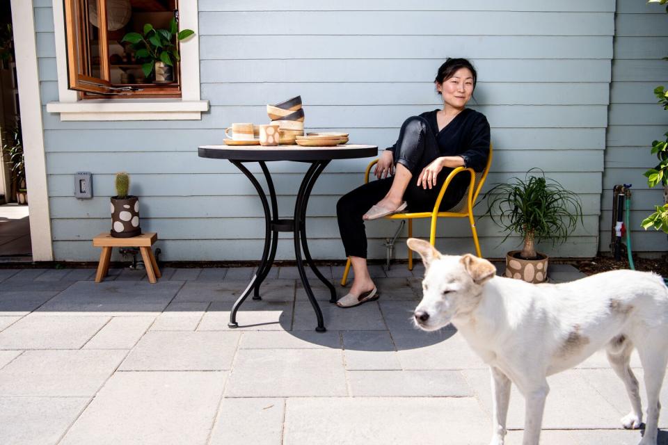 A woman is seated at a table outdoors with a dog to the right.