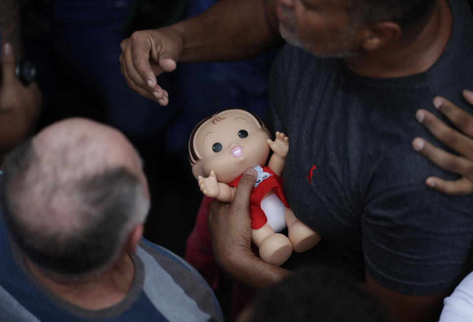 The grandfather of 8-year-old Ágatha Sales Felix holds her doll as she's buried at the cemetery in Rio de Janeiro, Brazil, Sunday, Sept. 22, 2019. Félix was hit by a stray bullet Friday amid what police said was a shootout with suspected criminals. However, residents say there was no shootout, and blame police. (AP Photo/Silvia Izquierdo)