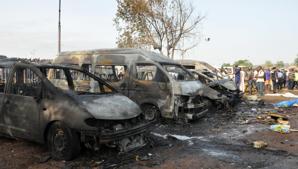 People gather at the site of a blast at the Nyanya Motor Park, about 16 kilometers (10 miles) from the center of Abuja, Nigeria, Monday, April 14, 2014. An explosion blasted through a busy commuter bus station on the outskirts of Abuja before 7 a.m. (0600 GMT) Monday as hundreds of people were traveling to work. (AP Photo/Gbemiga Olamikan)