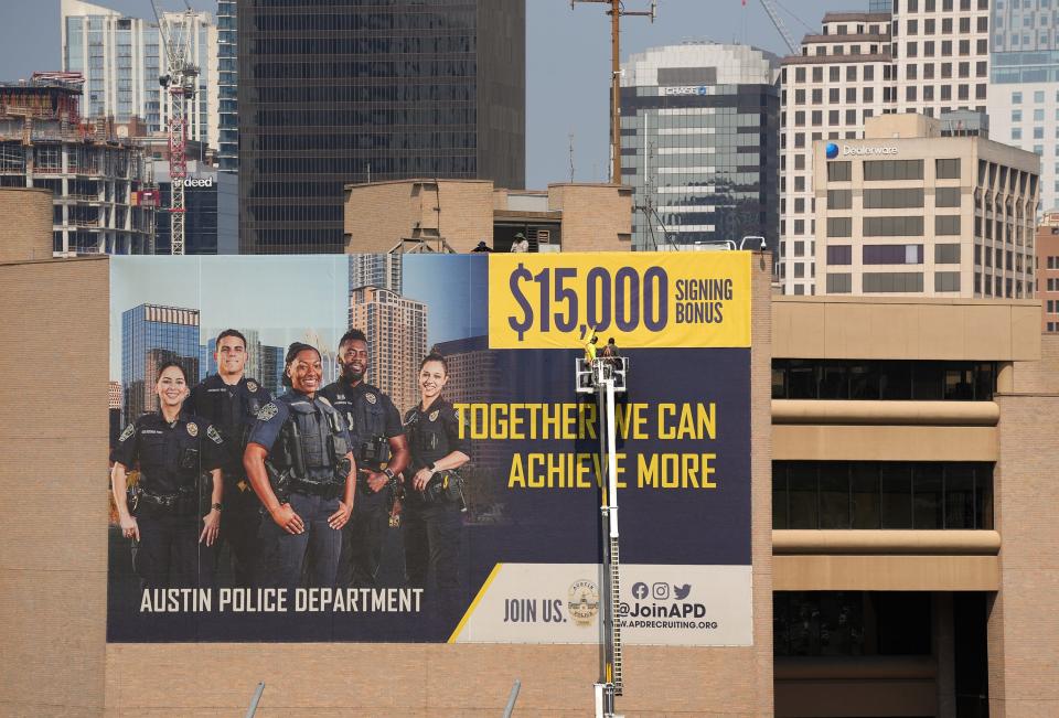 Workers install a large banner advertising a $15,000 signing bonus for Austin Police Department recruits at the downtown APD headquarters on Wednesday, June 21, 2023. The signing bonus is an effort to recruit highly qualified candidates to fill the record-high number of vacancies at the Austin Police Department.