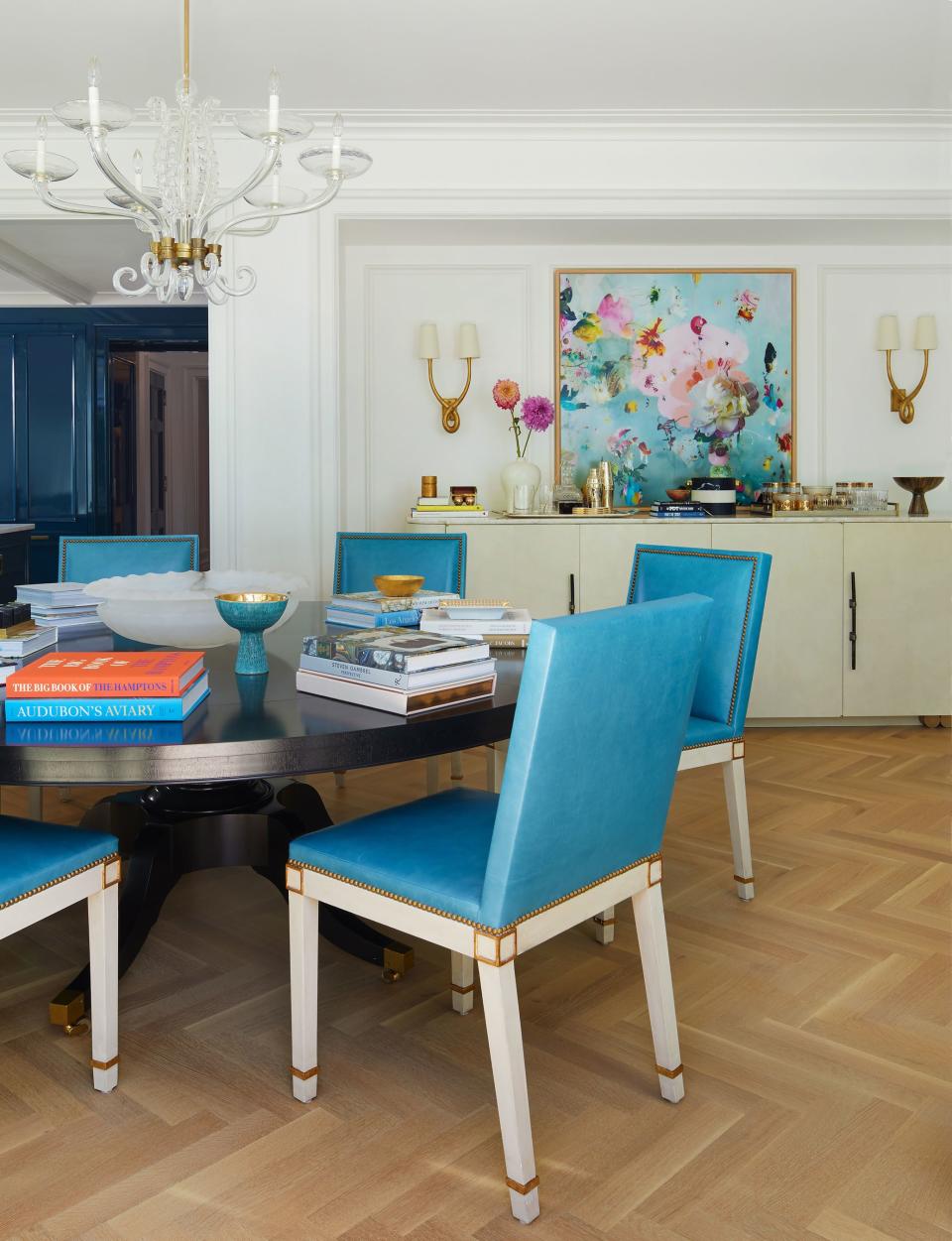In the dining area, custom chairs in a gesso finish with turquoise Italian leather surround a custom ebonized table under a 1940s Venini chandelier. Behind, an alcove holds the custom bar in a faux parchment finish with an Isabelle Menin photograph above it.