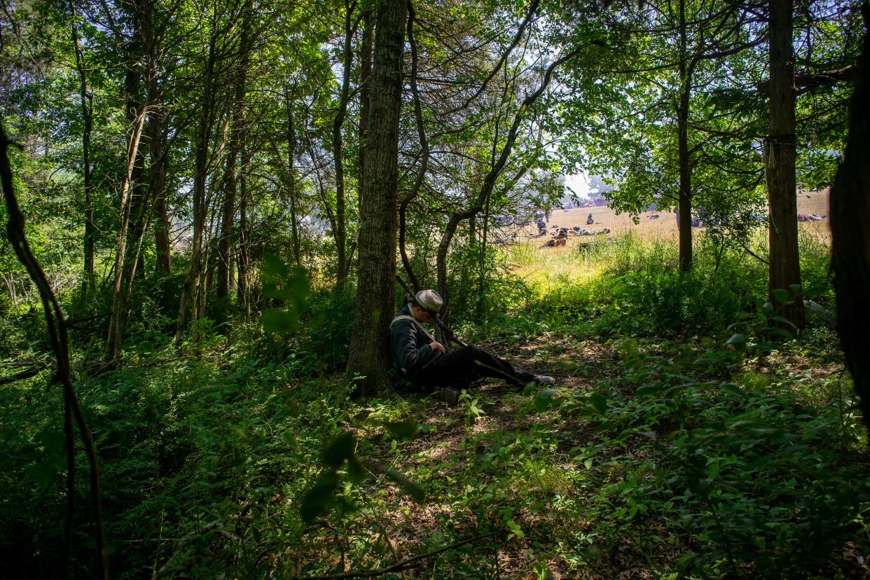 A person is seen playing dead while leaning up against a tree.