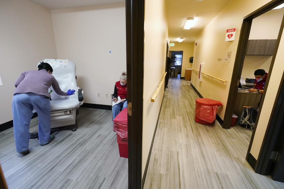 Dr. Cristina Toledo-Cornell, left, cleans a seat for the next patient as Dr. Dakotah Lane, right, works in his office as the Lummi National begins the first COVID-19 vaccinations Thursday, Dec. 17, 2020, on the Lummi Reservation, near Bellingham, Wash. Medical worker Melissa Fitzgerald, center, fills out paperwork before receiving her shot. The Native American tribe began rationing its first 300 doses of vaccine as it fights surging cases with a shelter-in-place order. (AP Photo/Elaine Thompson)