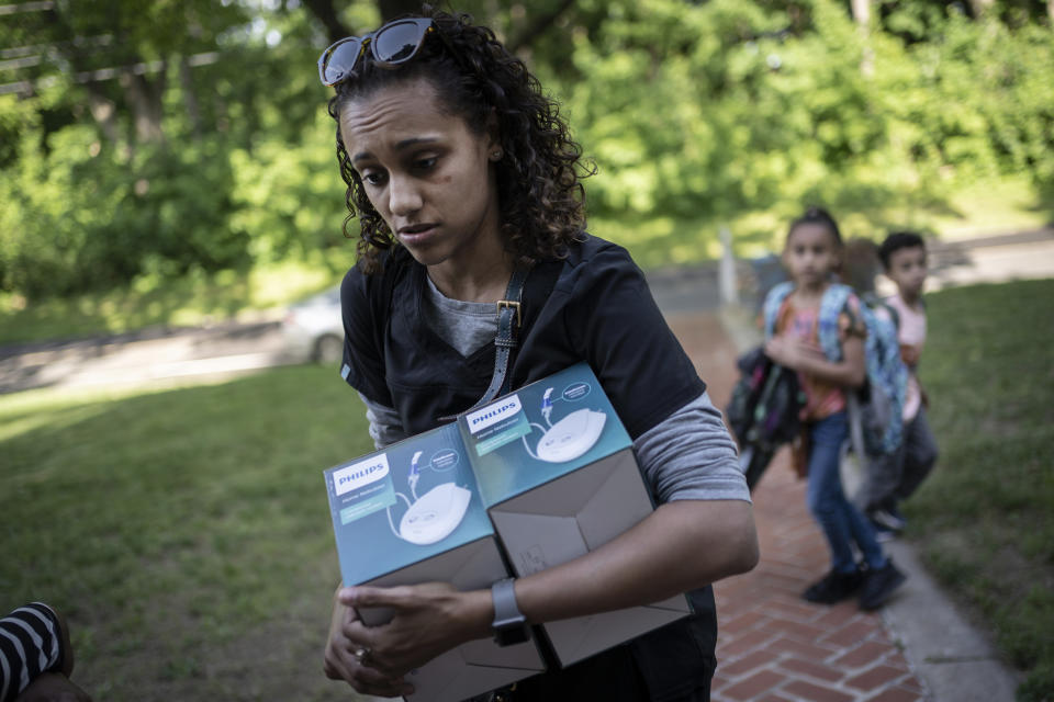 Catherine Manson unloads home nebulizer units from her car while her children, Caydence Manson, center, and Carter Manson, follow behind after they were picked up from school in Hartford, Conn., on Wednesday, May 25, 2022. All three of them suffer from asthma. The children have missed weeks of school, leaving them behind in schoolwork at a critical juncture for their education. And in turn, their parents were forced to miss work to care for them – putting a strain on the family’s finances. (AP Photo/Wong Maye-E)