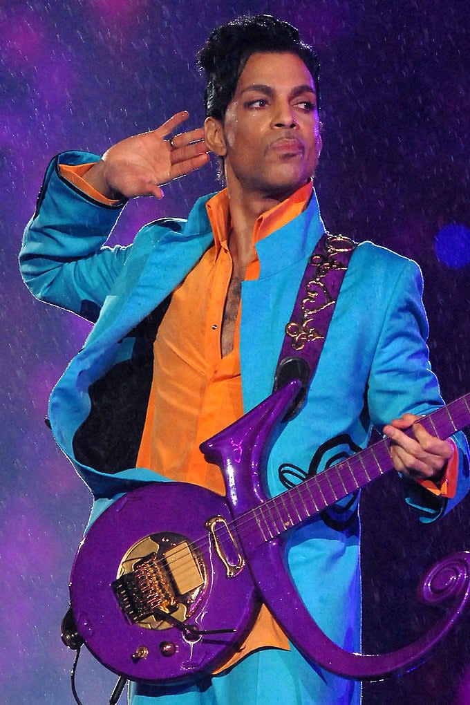 Performing artist in a teal and orange outfit with a purple guitar on stage