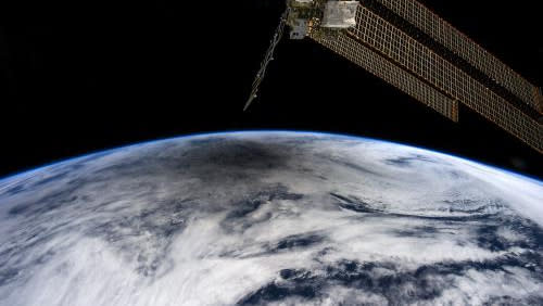  A round shadow falls on the top of a rounded Earth from space, Solar panels from the space station protrude from above. 