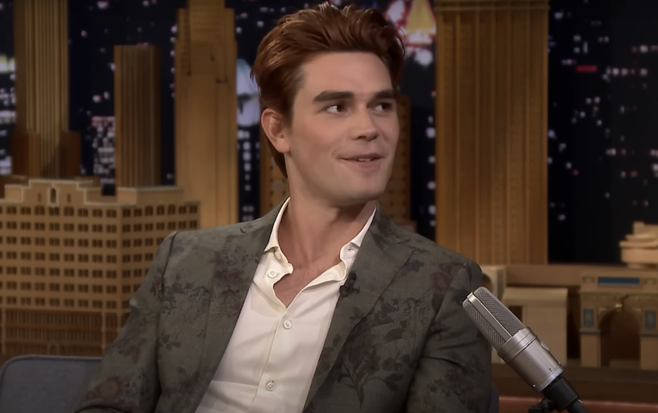 KJ Apa in a floral-patterned suit jacket and plain shirt, smiling and talking during a TV interview