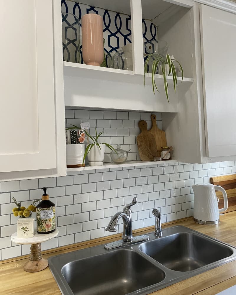 kitchen with pale gray cabinets, white subway tile backsplash, and black and white patterned wallpaper after makeover