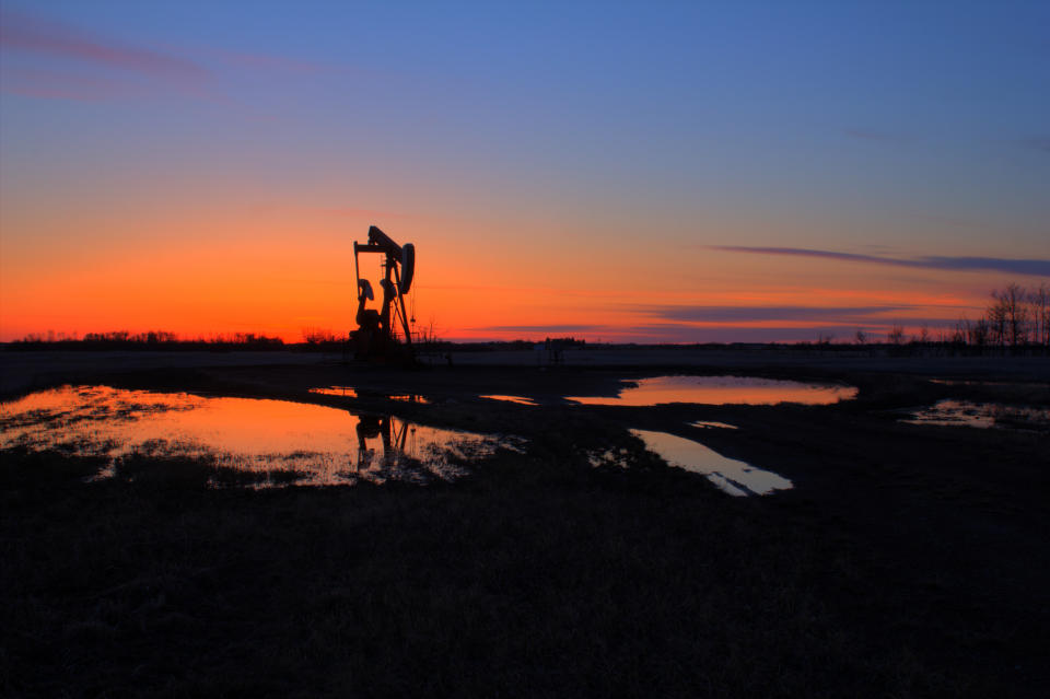 Pump jack backlit by the setting sun after rain.