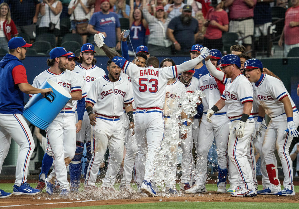 Texas Rangers' Adolis Garcia (53) is congratulated by teammates at home plate after hitting a walkoff home run off Washington Nationals relief pitcher Kyle Finnegan during the ninth inning of a baseball game Saturday, June 25, 2022, in Arlington, Texas. (AP Photo/Jeffrey McWhorter)