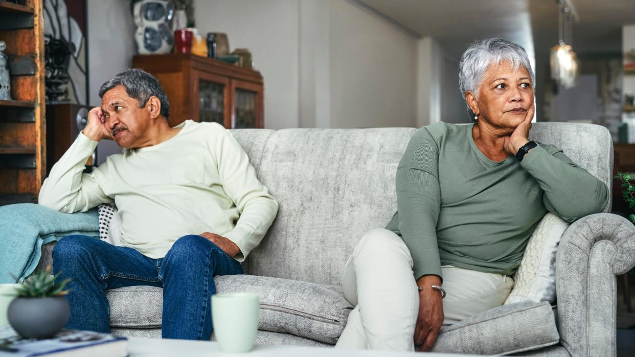  A senior couple sitting on opposite sides of the couch, having a disagreement. 