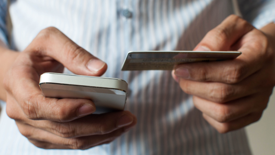 A man holding a smart phone and a credit card.