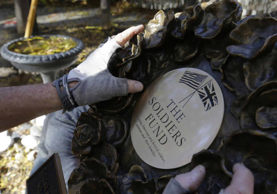 In this Wednesday, Nov. 7, 2018 photo James Re, of Boston, hands only, positions a bronze wreath as it becomes part of a memorial on the grounds of Old North Church, in Boston, that honors fallen soldiers from the U.S. and Britain. The memorial is being dedicated this month at an ironic venue - the Boston church where America's war for independence from England basically began. On Nov. 17, British and American military brass will unveil the bronze wreath and plaque at the church, saluting troops from both countries who have died in Iraq and Afghanistan. (AP Photo/Steven Senne)