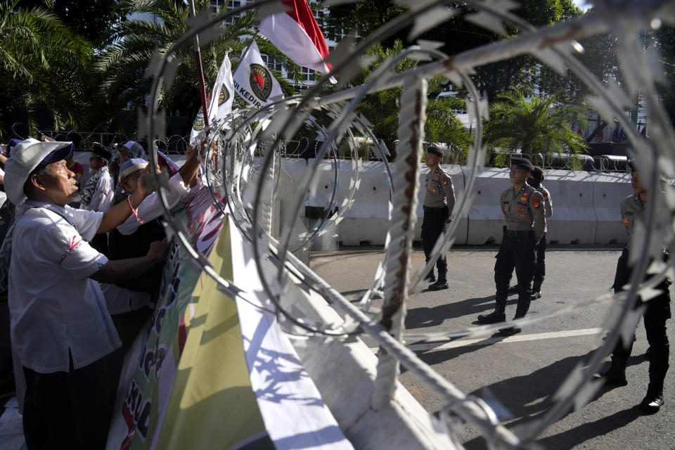 Protesters put up flags and posters on a razor wire barricade as police officers stand guard during a rally alleging a widespread fraud in the Feb. 14 presidential election, outside the General Election Commission's office in Jakarta, Indonesia, Wednesday, March 20, 2024. Presidential frontrunner Prabowo Subianto, a former general linked to past human rights abuses and his running mate Gibran Rakabuming Raka, the eldest son of Indonesian President Joko Widodo, are currently leading the tally with nearly 60% of the votes. (AP Photo/Dita Alangkara)