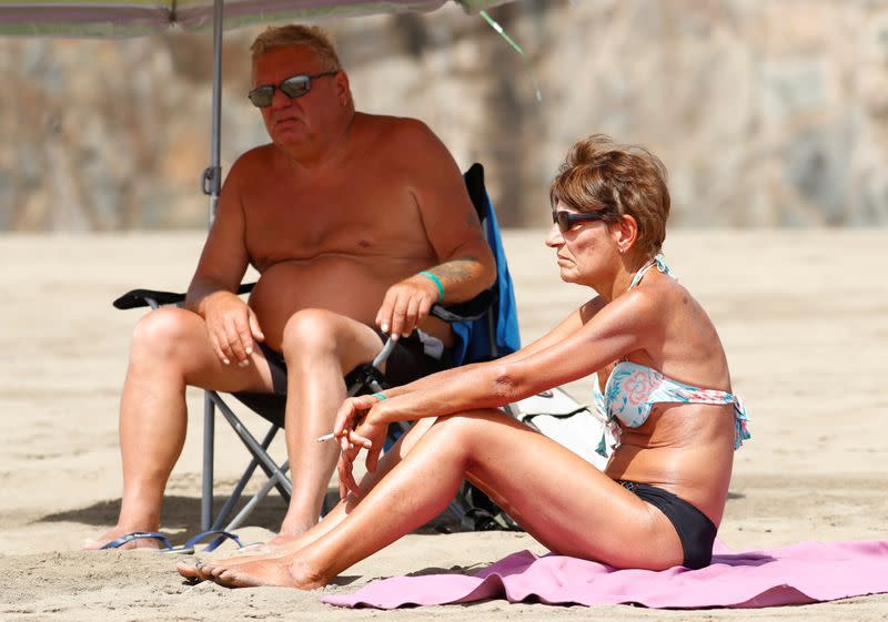 FILE PHOTO: A woman smokes a cigarette while sunbathing on the beach, as the regional government of the Canary Islands forbids smoking without maintaining a safe distance