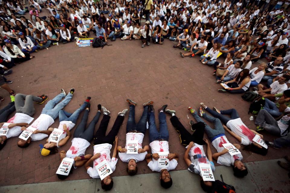 Demonstrators lie on the ground holding statistics about the people murdered in the 14 years of Chavista government, at a protest in Caracas, Venezuela, Friday, March 7, 2014. Venezuela is coming under increasing international scrutiny amid violence that most recently killed a National Guardsman and a civilian. United Nations human rights experts demanded answers Thursday from Venezuela's government about the use of violence and imprisonment in a crackdown on widespread demonstrations. (AP Photo/Fernando Llano)