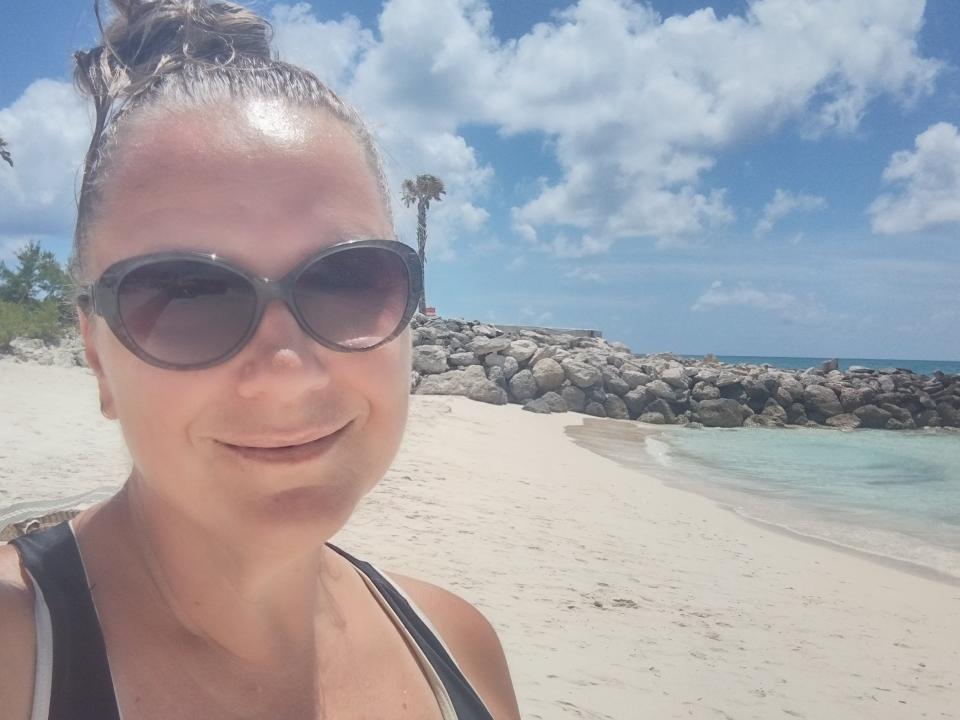 Woman wearing black sunglasses smiling for as selfie on a beach