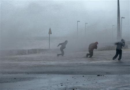 People run through sea spray in Rhyl, north Wales December 5, 2013. REUTERS/Phil Noble