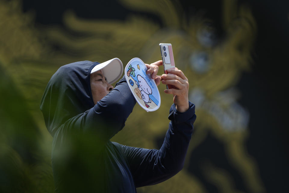 A woman uses a smartphone to film the Dragon Boat festival at a canal in Tongzhou, on the outskirts of Beijing, Monday, June 10, 2024. The Duanwu festival, also known as the Dragon Boat festival, falls on the fifth day of the fifth month of the Chinese lunar calendar and is marked by celebrations like eating rice dumplings and racing dragon boats. (AP Photo/Andy Wong)