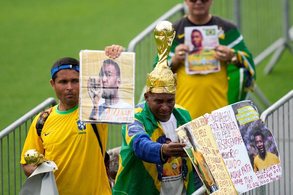 Fans hold up photos of the late Brazilian soccer great Pele as they line up at Vila Belmiro stadium