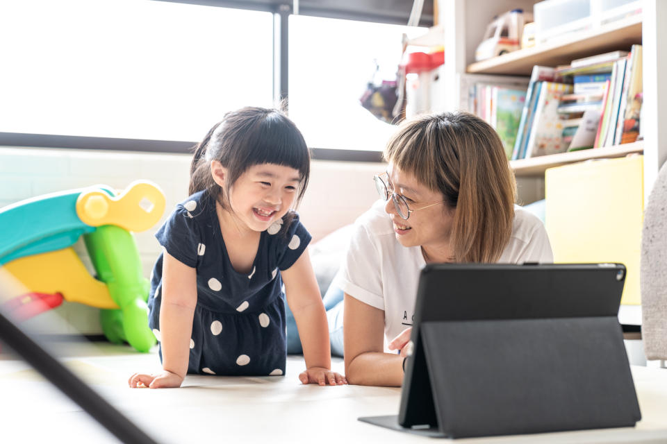 Mother using tablet watching videos happily with young daughter at living room.