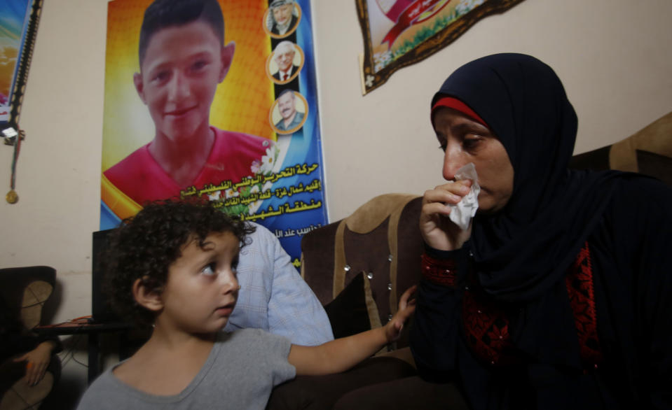 In this Tuesday July 2, 2019 photo, Raeda, mother of 14-year-old Mohammed Ayyoub, sits near a poster with his photo, at the family home in Jabaliya refugee camp. Mohammed was killed during a protest on the fence separating Israel and Gaza in 2018. The Israeli military has opened investigations into 24 potentially criminal shootings of Palestinians in the West Bank and Gaza Strip, but none have yielded indictments and rights groups say little effort is made to gather evidence or interview witnesses. (AP Photo/Hatem Moussa)