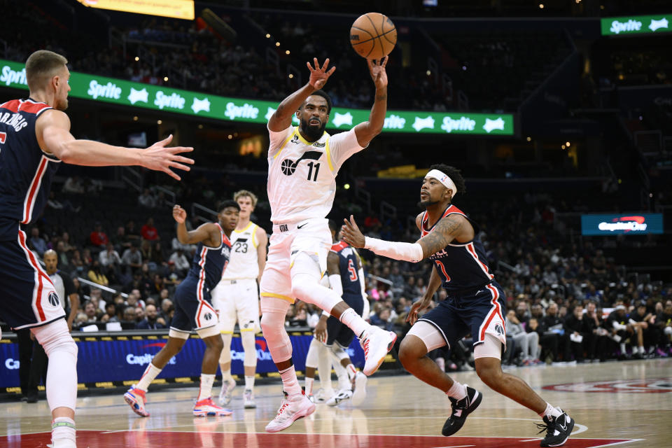 Utah Jazz guard Mike Conley (11) passes the ball away from Washington Wizards guard Jordan Goodwin, right, and center Kristaps Porzingis during the first half of an NBA basketball game Saturday, Nov. 12, 2022, in Washington. (AP Photo/Nick Wass)