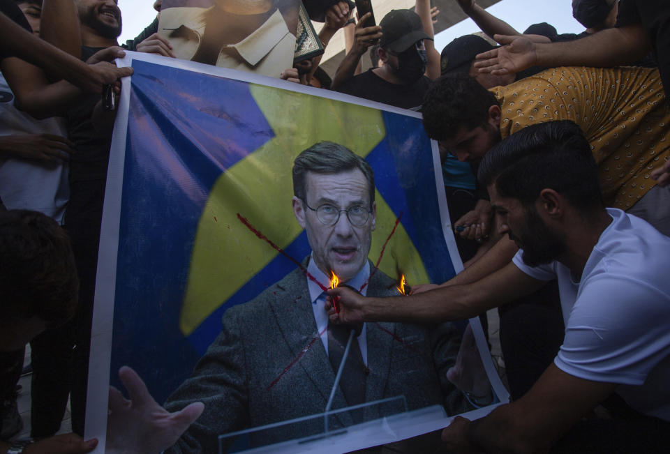 FILE - Iraqis burns the picture of Sweden's prime Ulf Kristersson, during a protest in Tahrir Square, Thursday، July 20, 2023 in Baghdad, Iraq. The targeting of Swedish citizens in an attack in Brussels on the night of Monday, Oct. 16, 2023 has shocked the Scandinavian country, yet the government had been warning for months that Swedes were at greater risk since a recent string of public desecrations of the Quran, Islam's holy book, by a handful of anti-Islam activists. (AP Photo/Adil AL-Khazali, File)