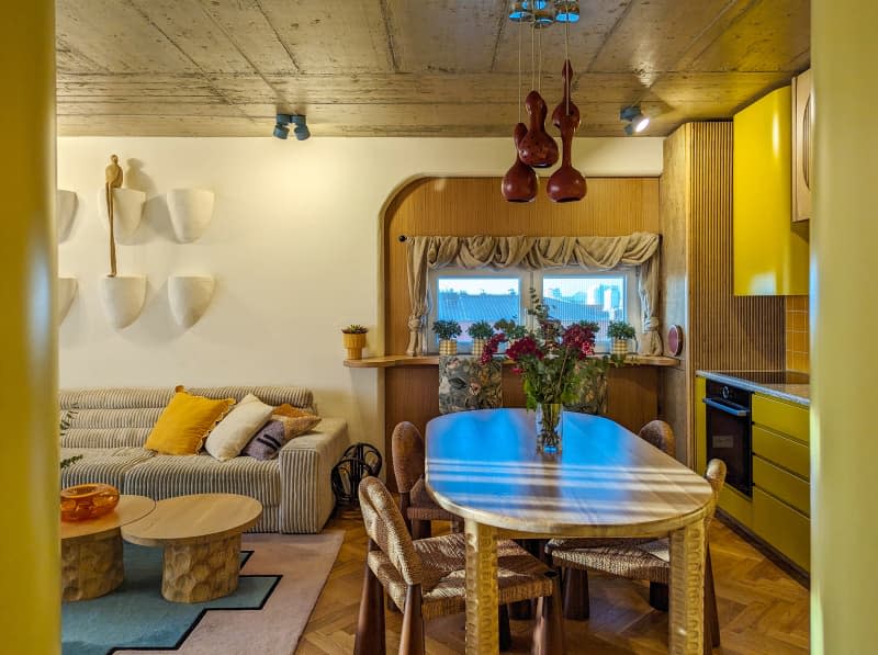 Yellow kitchen with fluted wood cabinets, parquet floor, window bar and dining table. Living room to the left