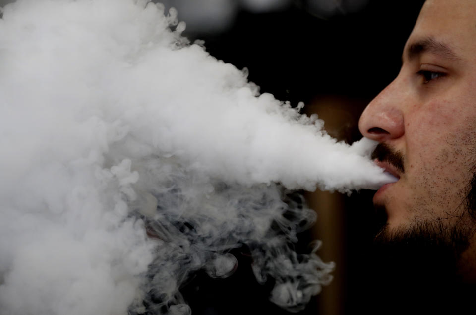 A man breathes vape from an e-cigarette at a vape shop in London, Friday, Aug. 17, 2018. A report by the British science and technology MPs committee suggest that rules around e-cigarettes should be relaxed to help accelerate already declining smoking rates. (AP Photo/Frank Augstein)