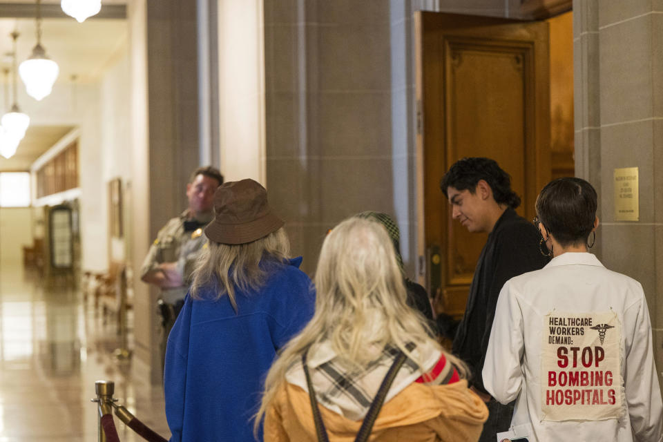 Emma Chew Murphy, wearing a sign on her jacket, waits in line to speak during public comment at the San Francisco Board of Supervisors meeting in San Francisco, Monday, Jan. 8, 2024. The city's board of supervisors is taking up a controversial resolution calling for a sustained cease-fire in Gaza, a resolution that pro-Palestinian and Jewish peace groups have successfully pushed through in other cities. (AP Photo/Nic Coury)