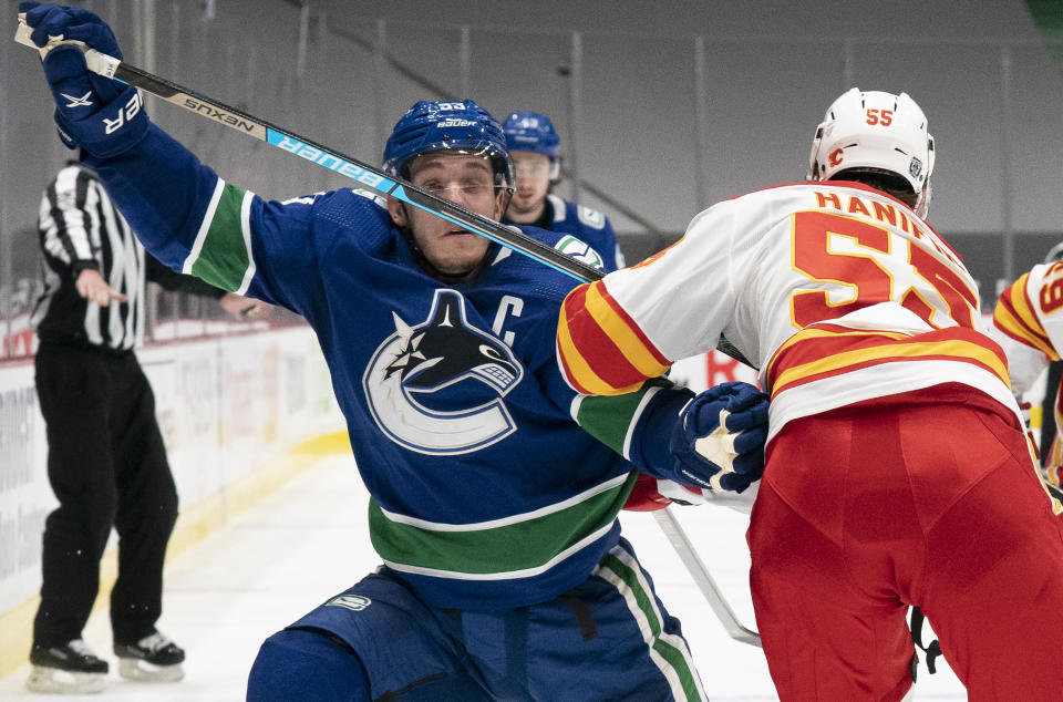 Vancouver Canucks center Bo Horvat (53) fights for control of the puck with Calgary Flames defenseman Noah Hanifin (55) during the second period of an NHL hockey game Thursday, Feb. 11, 2021, in Vancouver, British Columbia. (Jonathan Hayward/The Canadian Press via AP)