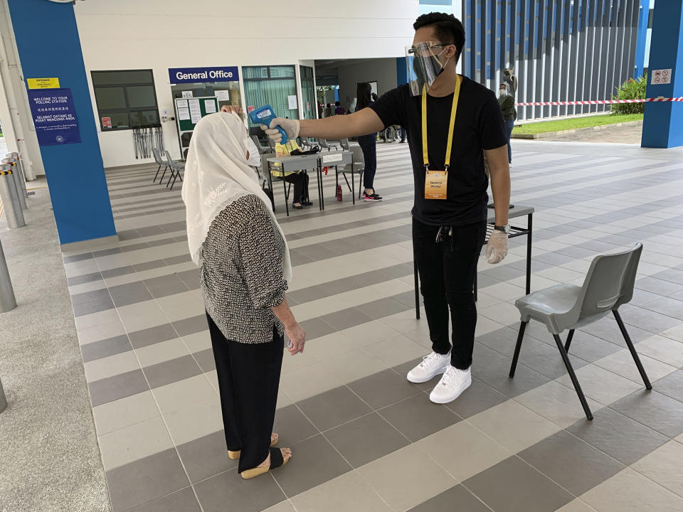 A voter, left, wearing a face mask has her temperature checked with a thermal scanner at the Dunearn Secondary School polling station in Singapore Friday, July 10, 2020. Wearing masks and plastic gloves, Singaporeans began voting in a general election that is expected to return Prime Minister Lee Hsien Loong's long-ruling party to power. (AP Photo/Royston Chan)