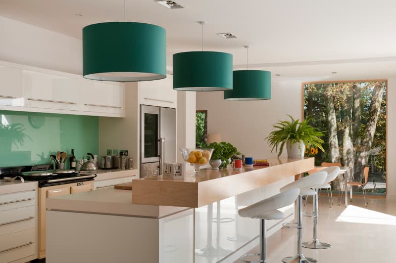 Above the kitchen's Silestone worktop, which has a high bar and stools, are three green pendant lights above the units.