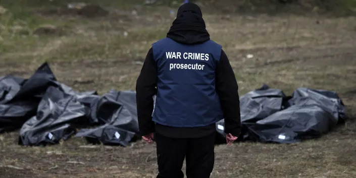A War Crimes prosecutor looks at bodies in black plastic bags pulled from a mass grave behind a church in Bucha on April 11