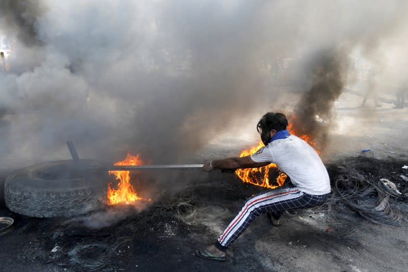 An Iraqi demonstrator pulls a burning tire as he blocks the road during ongoing anti-government protests, in Baghdad